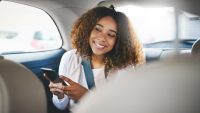 Shot of a young woman using her cellphone while sitting in the backseat of a car