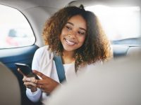 Shot of a young woman using her cellphone while sitting in the backseat of a car
